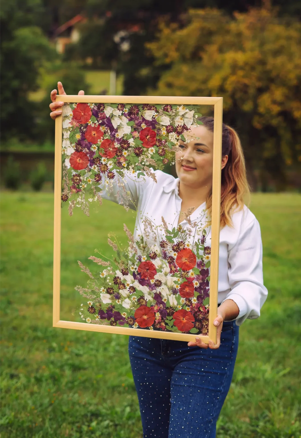 Autorka drží hotový obraz z lisovaných svatebních květin na zeleném pozadí